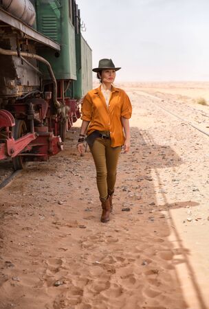 A cowboy girl is walking on the sand next to a vintage train. Shot in Jordan in the Wadi Rum desert in March 2020.の写真素材