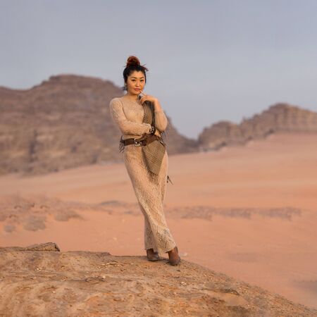 Beautiful Asian girl in a translucent flesh-colored long dress stand on a rock on the background of the lifeless Wadi Rum desert. Shot in Jordan.の写真素材