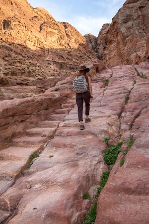Girl hiking tourist with a backpack and a cowboy hat climbs an ancient stone staircase carved from stone in the mountains.の写真素材