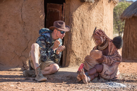 Namibia, Africa, Himba village, July 18, 2019: a Himba woman with an unusual hairstyle sits outside...