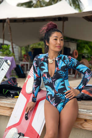 A beautiful brunette girl, a kitesurfer in excellent sports form, resting after skating, leaning on the boardの写真素材