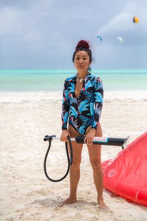 Beautiful sexy kitesurfing girl stands with a pump near her kite on the beach against the background of the turquoise seaの写真素材