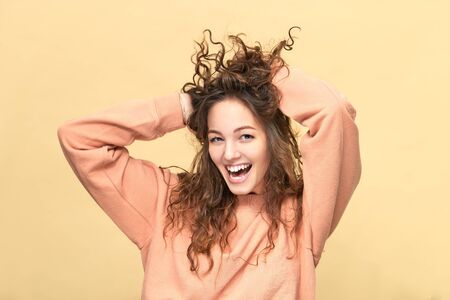 Portrait of a young beautiful woman wearing sweatshirt ruffling hair with her hands isolated over...
