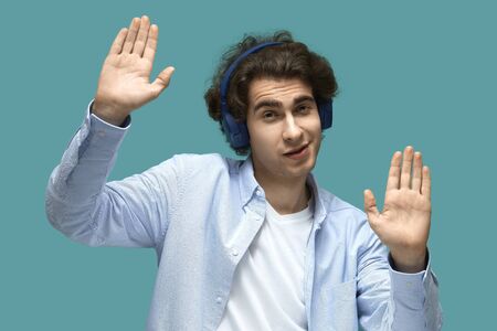 Portrait of a young beautiful man wearing white t-shirt and blue shirt in blue headphones. dancing...