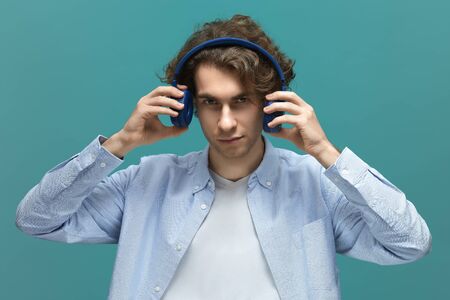 Portrait of a young beautiful man wearing white t-shirt and blue shirt take off a blue headphones...