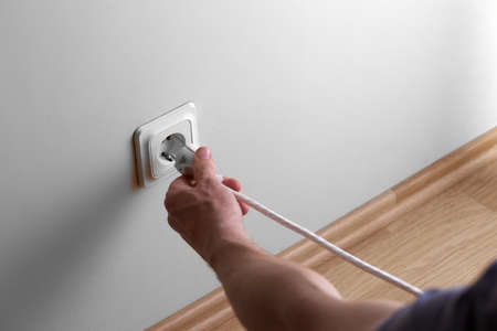 Man hand tyr to plugging electric plug a in a socket on the wall at low height from the floor but...