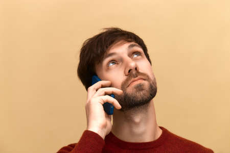 Photo of young man has phone conversation, holds mobile phone near ear, tells news to friend,...
