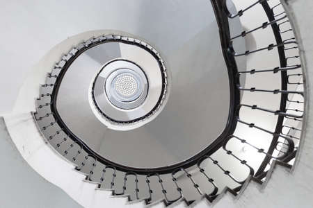 Black and white round spiral staircase with black railings with patterns top view at center