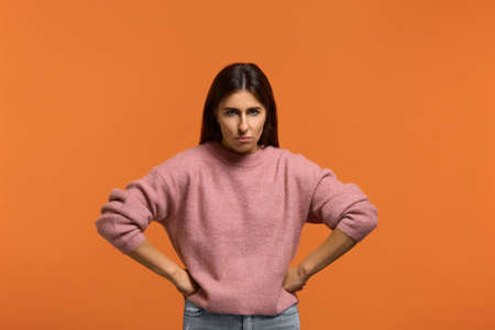 I'm very angry. Portrait of serious woman in pink sweater, holding hands on hip, frowning, having...