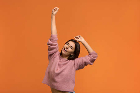 Photo of lively charming woman in knitted pink sweater dances joyfully and celebrates good news,...