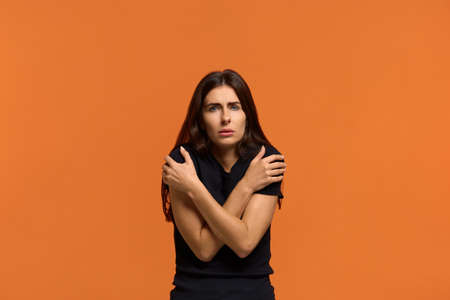 Desperate caucasian woman in black t-shirt trembles and feels cold, hugs herself to warm up, clatter...