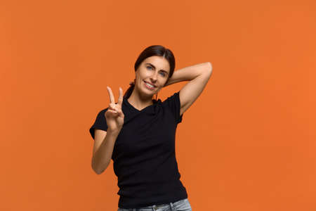 Nice to meet you. Beautiful caucasian woman in black t-shirt smiles broadly and gives peace sign,...
