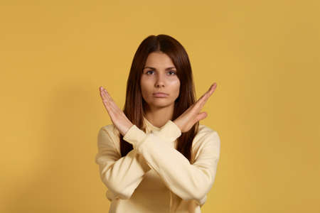 Cant go further. Serious caucasian woman in yellow hoodie keeps arms crossed, makes stop or ban...