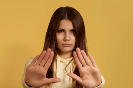 Thats enough. Portrait of serious strict caucasian woman in yellow hoodie makes stop sign, has...