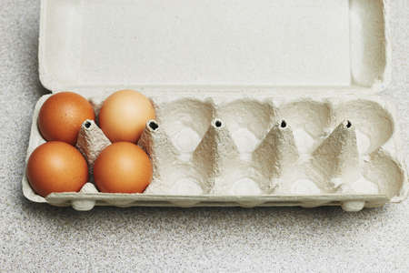 Culinary class in a kitchen. Four tinted brown chicken eggs in an open carton box for twelve eggs on...