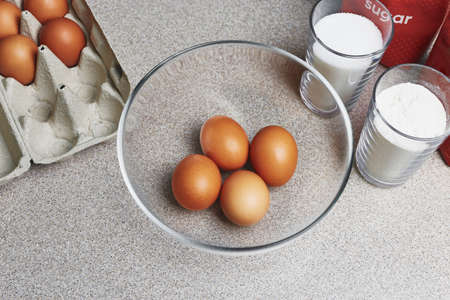 Ingredients for baking cake on a table. Cooking set. Open box with tinted brown chicken eggs, four eggs in a transparent bowl, flour, pack of sugar.Culinary class in a kitchenの写真素材