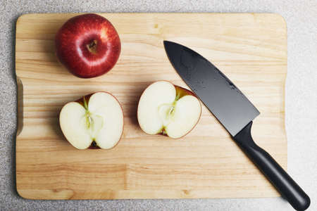 Cutting board with two red apples and a knife on it. One apple is whole, another one is cut, ready...
