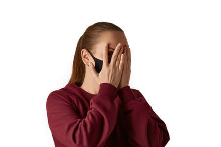 Scare but interesting. Young european woman wears face mask and burgundy sweatshirt, closes eyes...