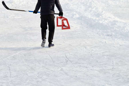 Teenager with hockey stick, wearing sneakers, goes to little training red goal on park ice rink....