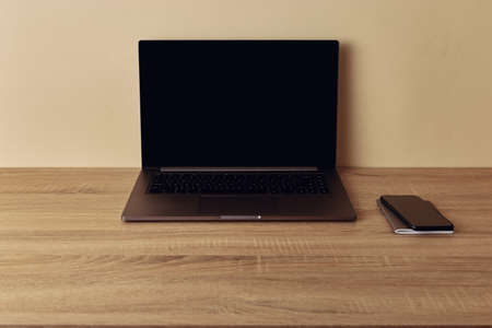 Workspace desk, laptop with blank screen, and mobile phone. Copy space on beige wallの写真素材