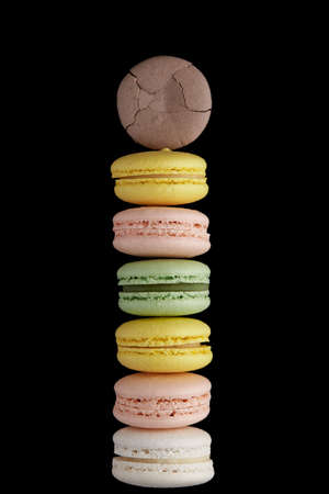 Macaroon. Stack of six colorful cake macaron with pastel tones and one cracked on black background. Top view of almond cookiesの写真素材