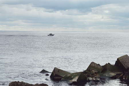 Motor boat sailing on sea, stones on foreground