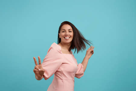 Cheerful smiling european woman with dark hair in pink dress dances, smiles broadly, feels lively...