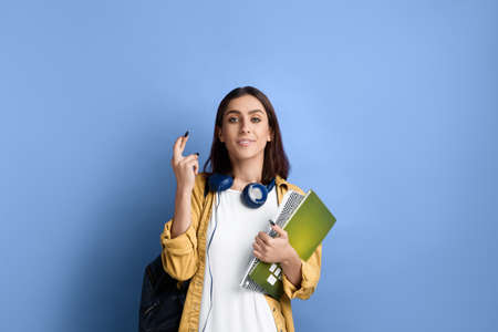 Positive smiling student girl is holding fingers crossed for passing an important exam, hopes for...