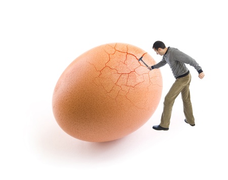Young man cracking an egg using a hammerの写真素材