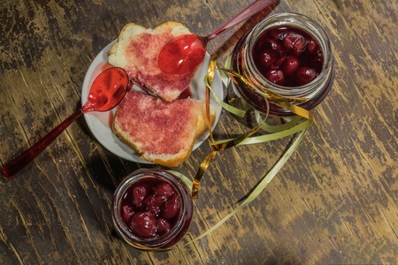 Cherry jam and white bread on wooden backgroundの写真素材