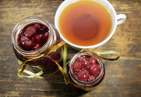Two jars cherry jam and a Cup of tea on a wooden table. Wooden backgroundの写真素材
