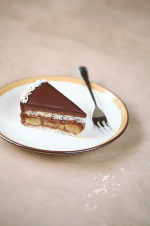 Piece of Chocolate, Coconut and Banana Cake on plate, on light beige background.