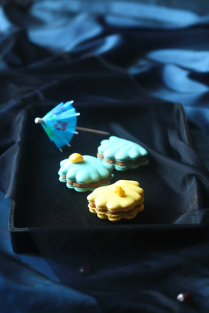 Blue and Yellow Seashell Macarons on black tray, on dark background.の写真素材