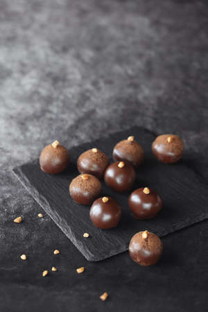 Handmade Chocolate Glazed Truffles, decorated with caramelized walnuts, on a black board, on a dark...