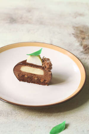 Chocolate Mousse Dome Cakes, covered with chocolate mirror glaze and yellow velvet spray-coated quenelle lemon mousse, garnished with green chocolate leaves and moss sponge, on light background.の写真素材