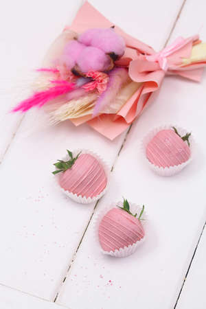 Pink Chocolate dipped Strawberries and Pink Dried Flowers Bouquet, on white wooden background.の写真素材