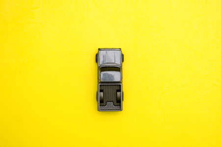 A close-up of a toy car on a yellow background. Lonely car made of metal view from above