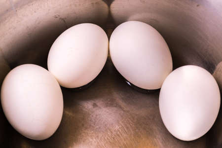 Four eggs lie in a saucepan. White eggs are boiled and cooled.