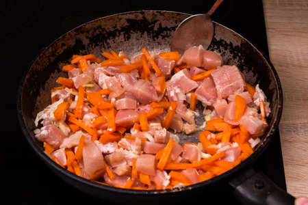 Pieces of chicken and carrots stew in a frying pan in oil. Cooking pilaf.の写真素材