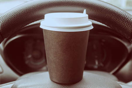A cardboard cup of coffee on the steering wheel of a car. Rest stop on the road. Have a quick snack in the car.の写真素材