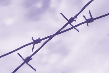 Old rusty barbed wire. Metal barbed wire fence close-up with blurred background. Blue and cloudy skyの写真素材
