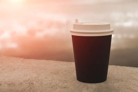 A cardboard cup of coffee on the background of a pond. Coffee to go.の写真素材