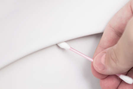 A hand wipes with a cotton swab under the rim of the toilet.の写真素材