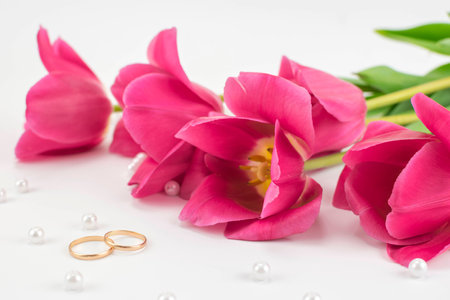 bouquet of red tulips, wedding rings, perfume and bead lying on a white backgroundの写真素材