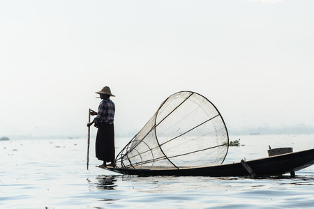 INLE LAKE, MYANMAR - FEBRUARY 15, 2014: Burmese fisherman on bamboo boat catching fish in traditional way with handmade net.のeditorial素材