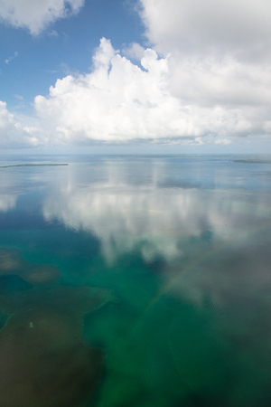 Aerial approach to Guadeloupe with mirrored cloudscapes in turquoise waterの写真素材