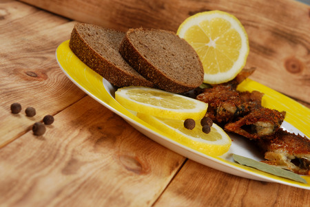 Grilled fish with lemon, bread, round pepper and bay leaf on a  plate on a wooden backgroundの写真素材