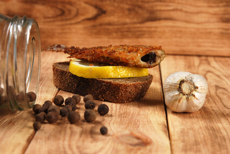 sandwich of rye bread with fried fish and lemon on a wooden backgroundの写真素材