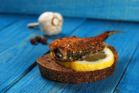 sandwich of rye bread with fried fish and lemon on a blue wooden background