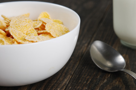 Corn flakes in small white bowls with a jar of yogurt and a spoon on a dark wooden backgroundの写真素材